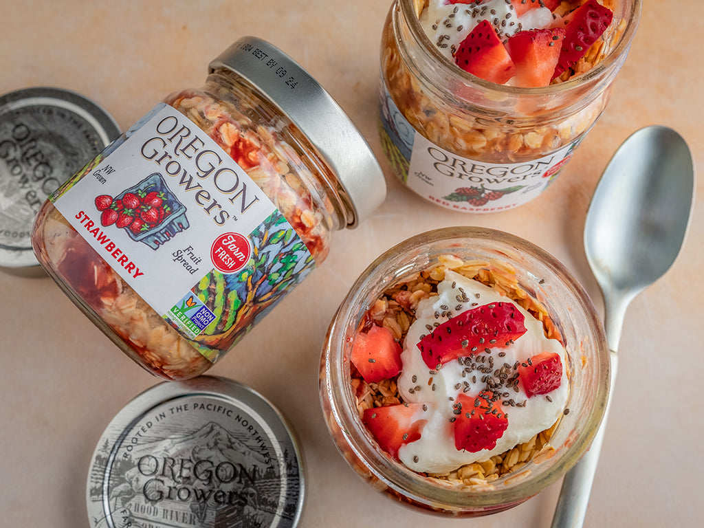 Top view of PB&J Overnight Oats recipe in a jar alongside Oregon Growers Strawberry Jam and Oregon Growers Honey on a table.