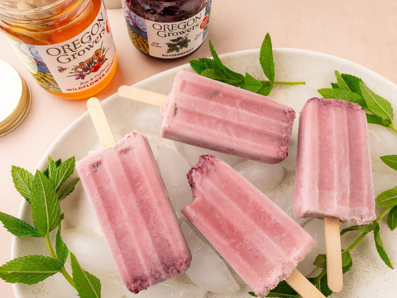 Top view of Boysenberry Mint Popsicles on a plate with Oregon Growers Boysenberry Jam and Wildflower Honey jars in the background.