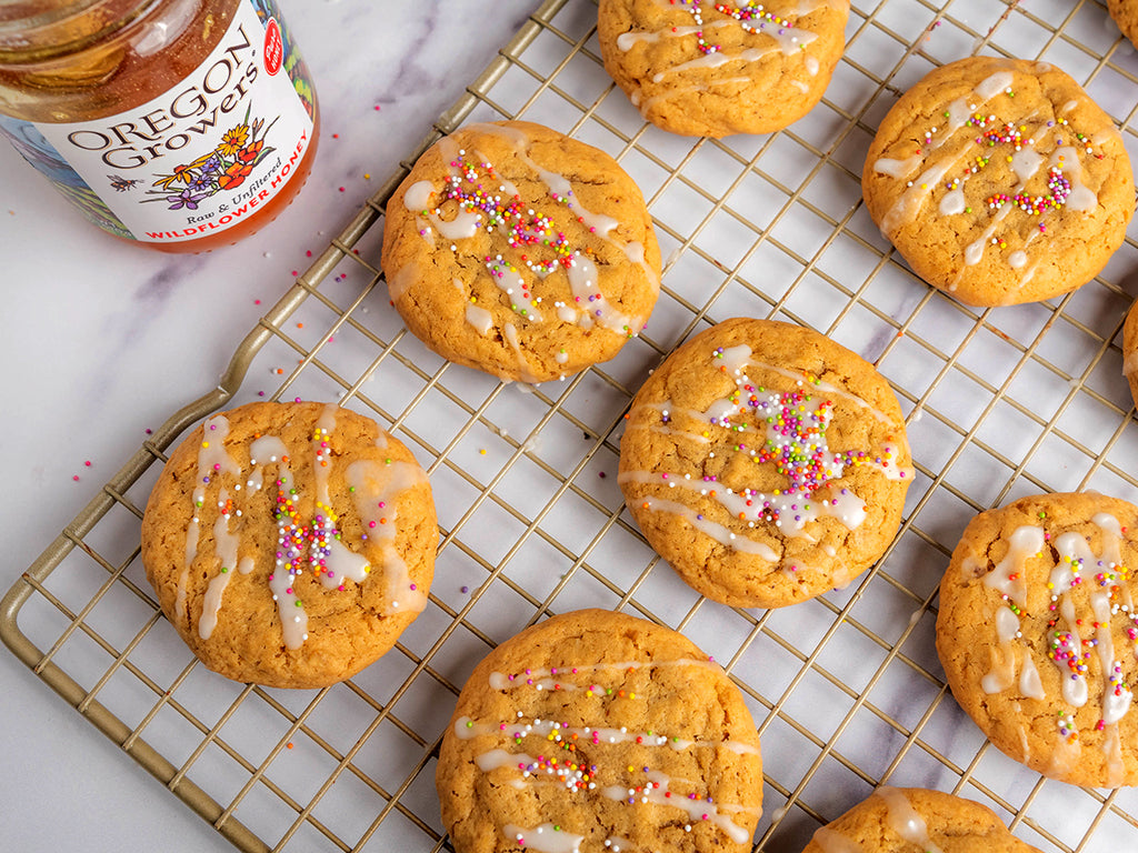 Top view of Browned Butter Honey Oat Cookies on a baking tray placed on a table, with an open jar of Oregon Growers honey beside the tray