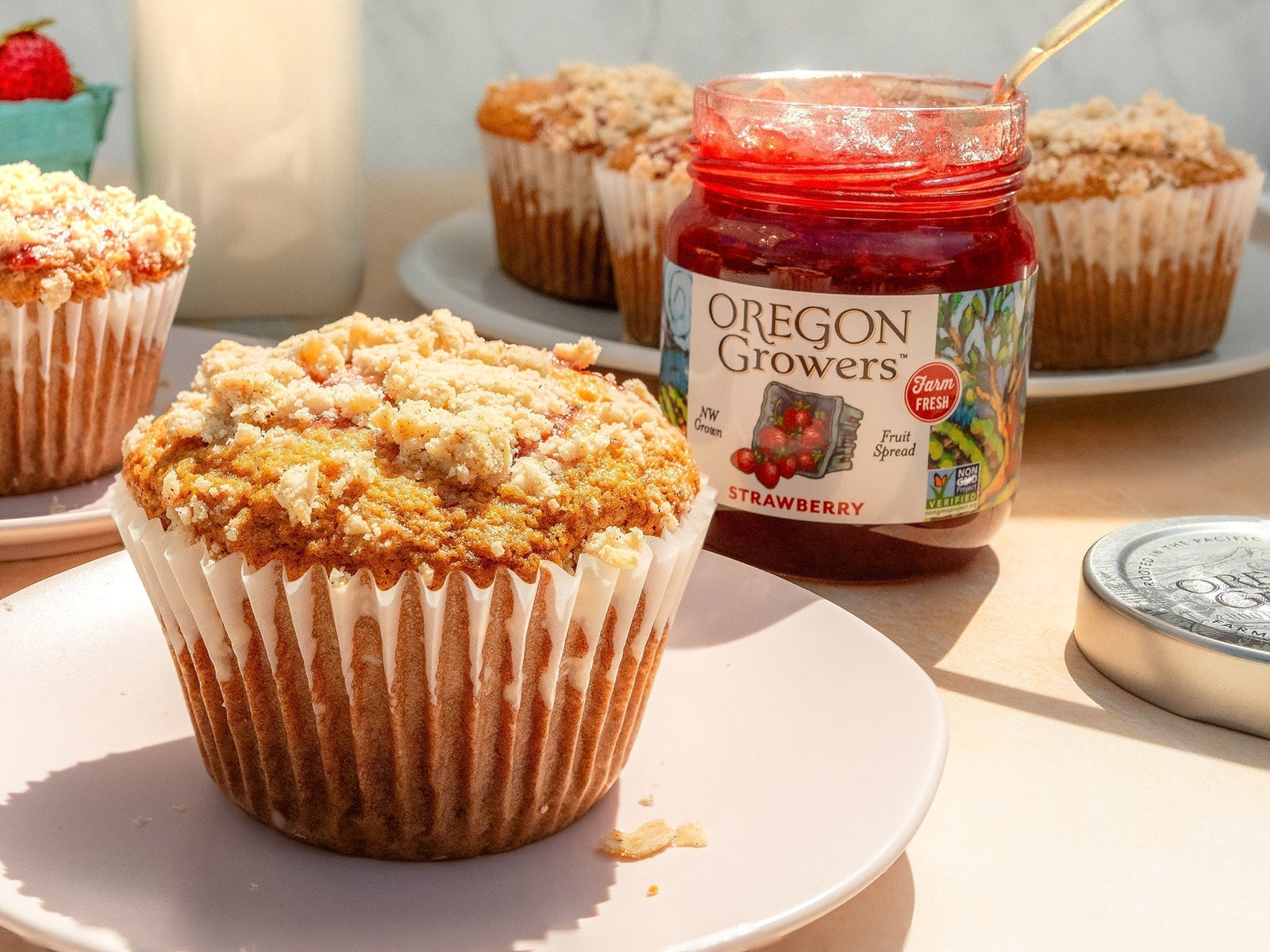 A Browned Butter Strawberry Muffin on a plate next to a jar of Oregon Growers strawberry jam
