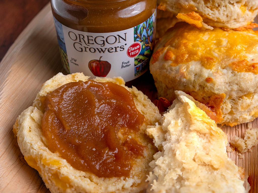 Closeup of Cheddar Biscuits with Apple Butter on a wooden serving platter with a opened jar of Oregon Growers Apple Butter.