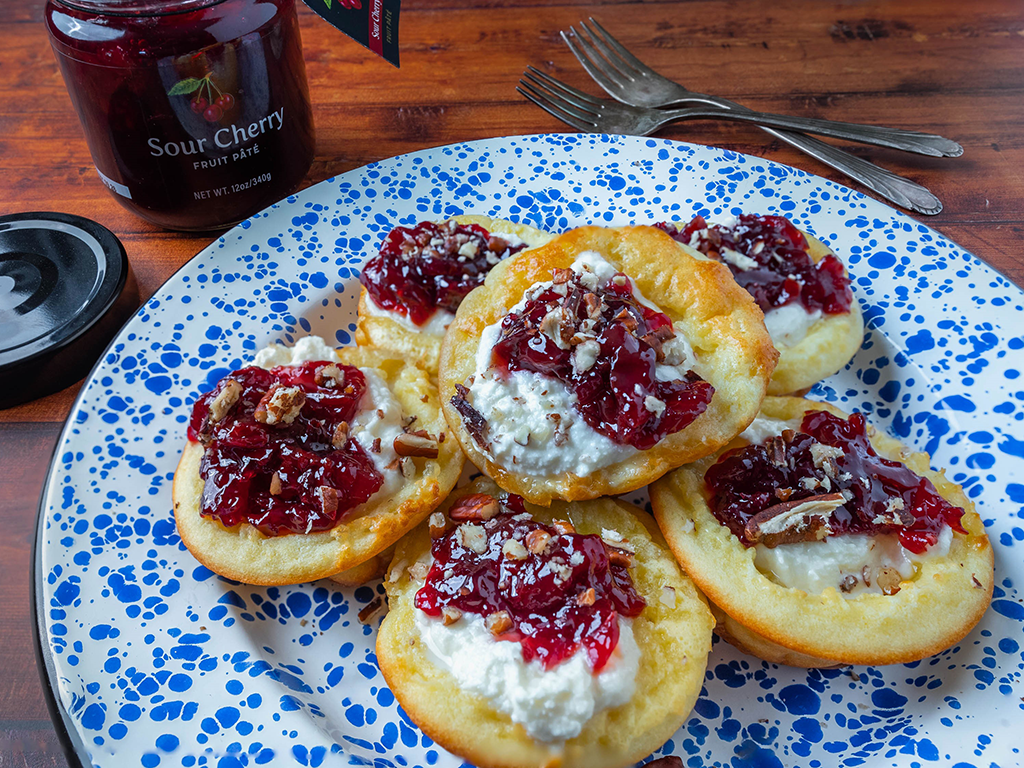 Top view of a plate containing Cherry Mini Dutch Baby Pancakes with an opened jar of Oregon Growers Sour Cherry Fruit Pate nearby.