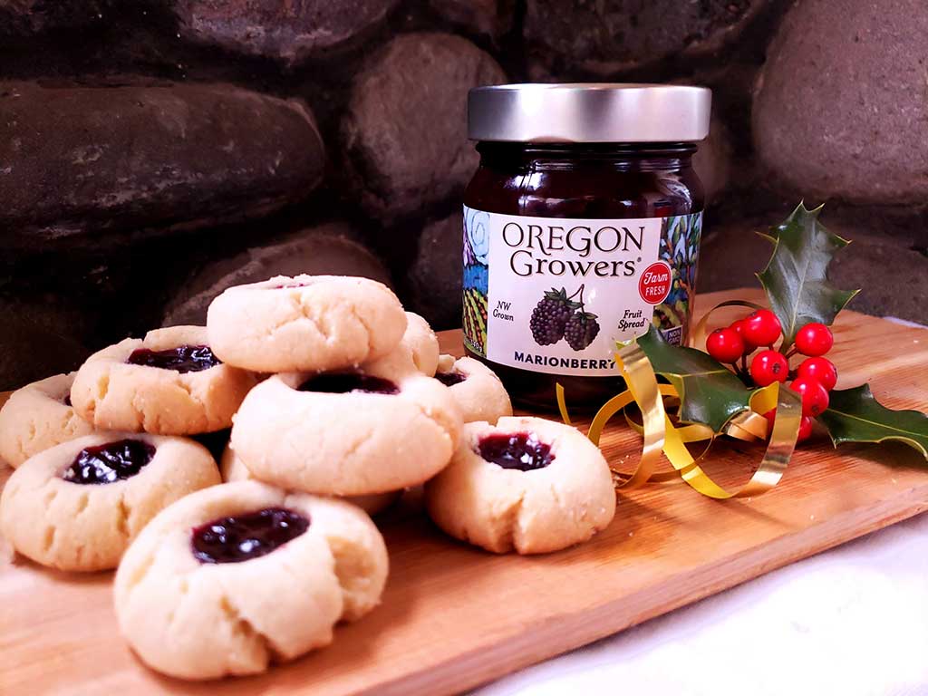 A serving platter stacked with Thumbprint Cookies and featuring a jar of Oregon Growers Marionberry Fruit Spread.