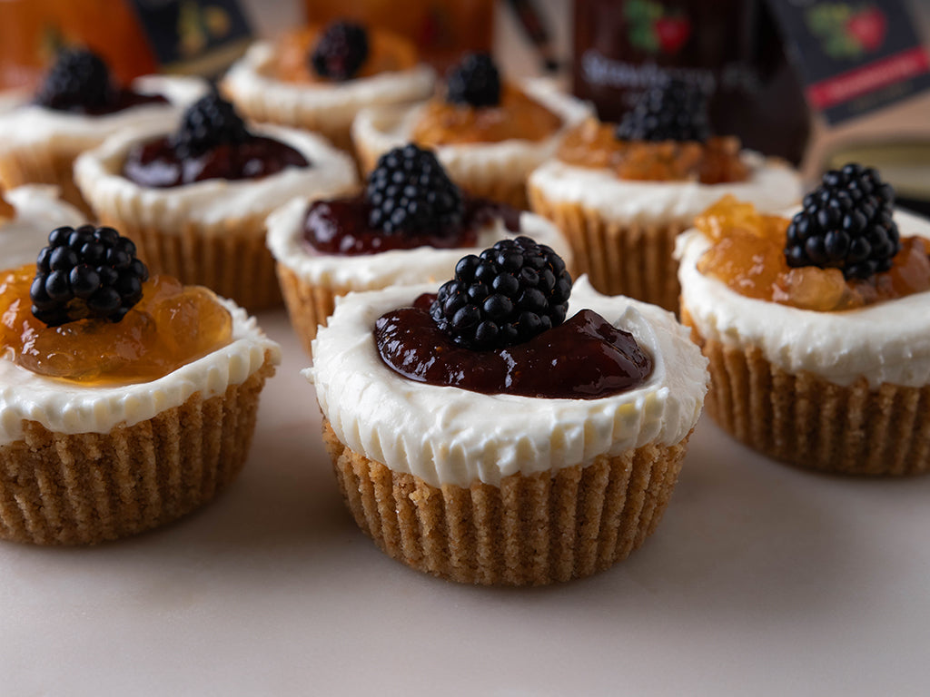 A table with no-bake mini ricotta cheesecakes scattered on top and jars of Oregon Growers Fruit Pates in the background.