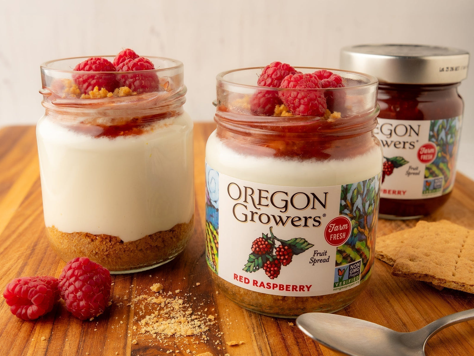 Three glass jars of Oregon Growers Red Raspberry Spread are shown on a wooden surface.