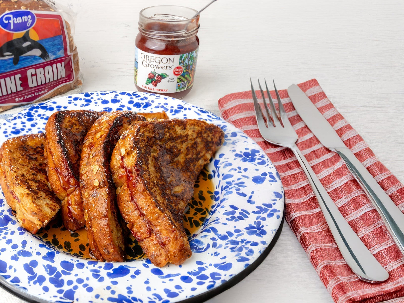 The PB&J French toast (a recipe by Oregon Growers)served on a blue and white plate with a jar of Oregon Growers Red Raspberry jam and a loaf of Franz Nine Grain bread.
