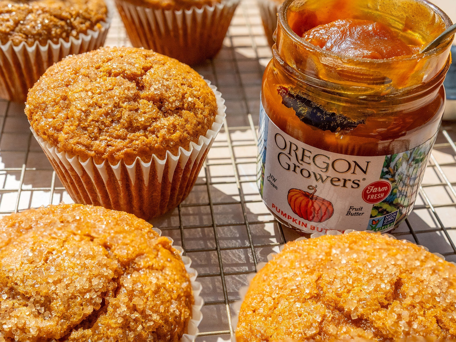 Pumpkin Butter Muffins with an opened jar of Oregon Growers Pumpkin Butter on a cooling rack.
