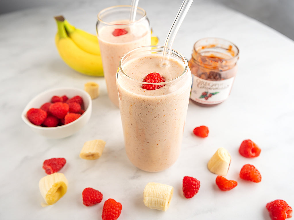 The Raspberry Jammer Smoothie on the breakfast table surrounded by fresh ingredients and a jar of Oregon Growers Red Raspberry Jam.