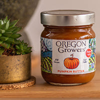 A close-up view of Oregon Growers Pumpkin Butter on a table sitting next to a decorative plant. 