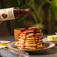 A bottle of our Raspberry Fruit syrup drizzling syrup onto a stack of pancakes.
