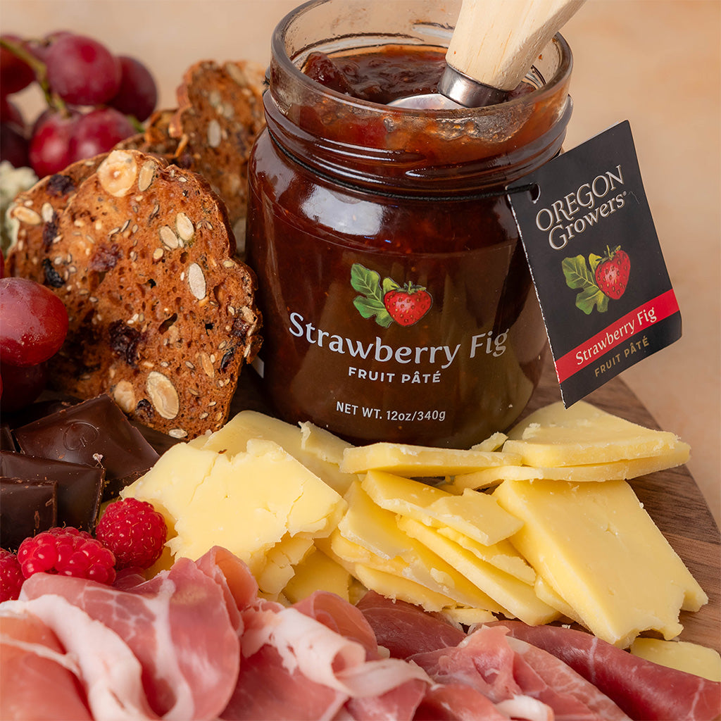 Close-up of Oregon Growers Strawberry Fig fruit pate jar in front of fruit, cheese, and other snacks.