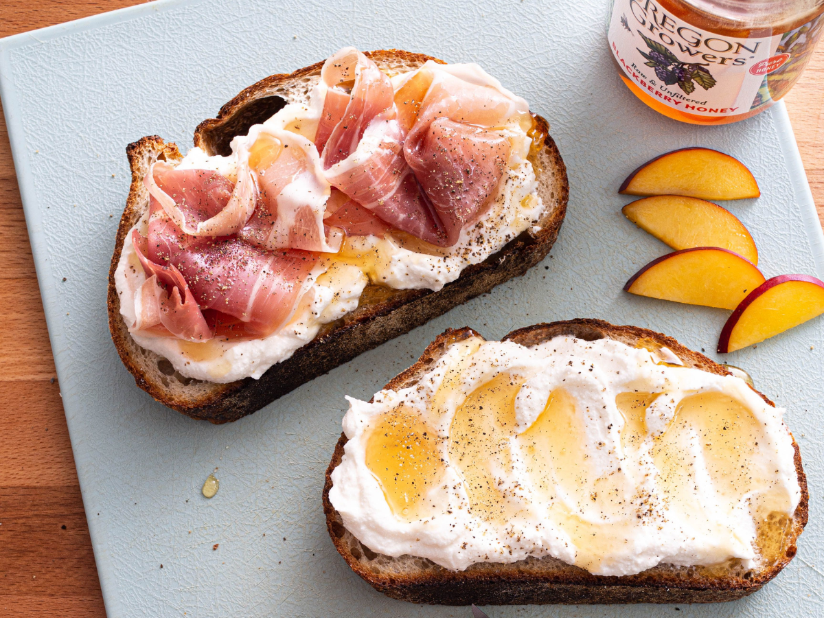 Top view of toast slices covered with creamy ricotta, ham, and fruit slices... drizzled with Oregon Grower's Honey.
