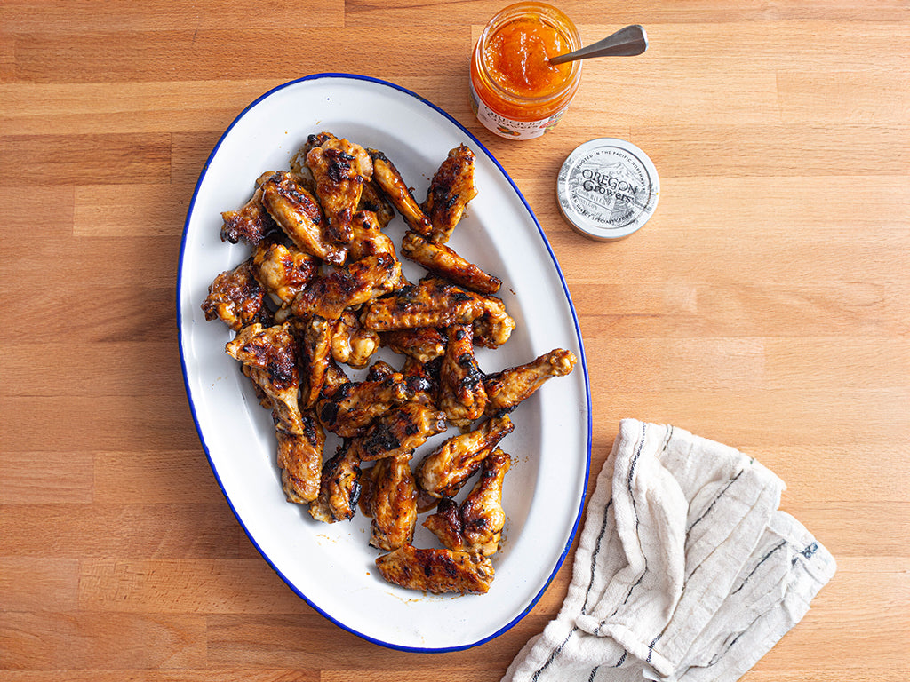 Tabletop view from above with a plate of Grilled Apricot Chicken Wings next to a jar of Oregon Growers Apricot jam.