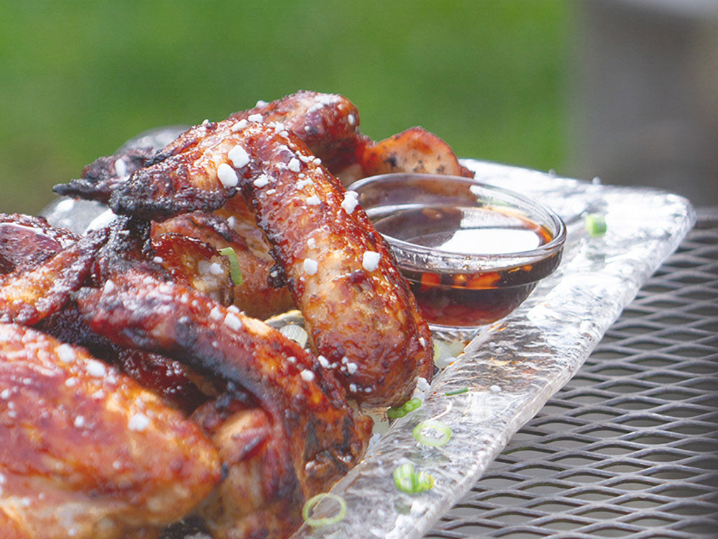 Close-up view of baked chicken wings being served on a platter and prepared with Marionberry Habanero Jam, seasoning, and garnish.