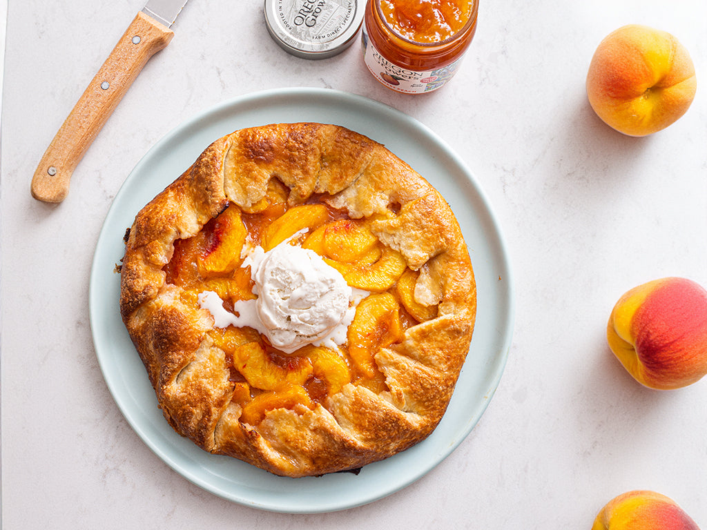 Top View of a table with Orchard Peach Galette Recipe on a plate next to a jar of Oregon Growers Peach Jam