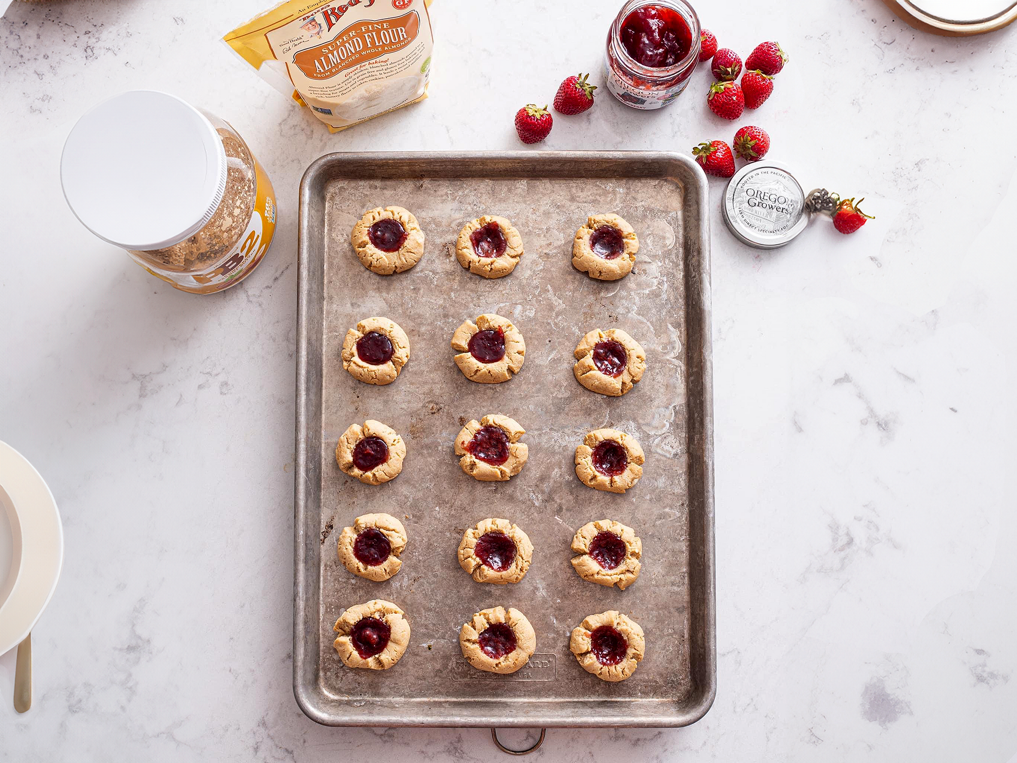 Peanut Butter and Strawberry Thumbprint Cookies on a cookie sheet with a jar of Oregon Growers Strawberry Jam and peanut butter  on the side.