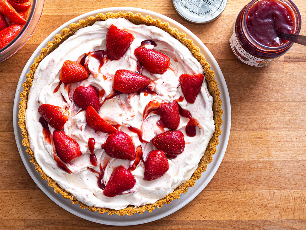 Tabletop view from above with a plate containing the Strawberry Rhubarb Cream Cheese Tart recipe next to a jar of jam.