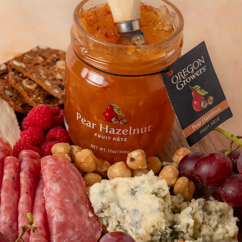 Close-up of Oregon Growers Pear Hazelnut fruit Pate jar in front of fruit, cheese, and other snacks.