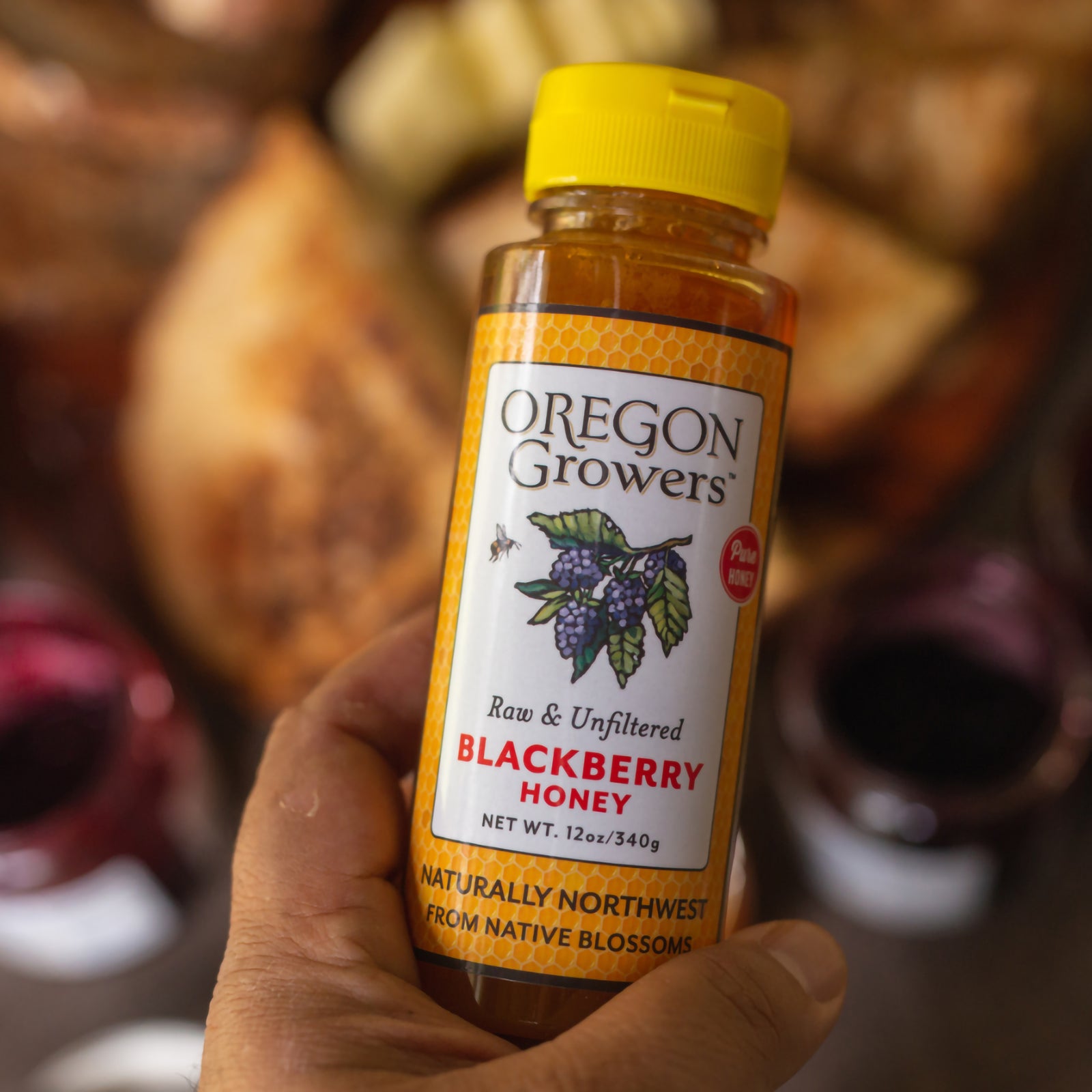 Close-up of a hand holding our 12 oz Blackberry Honey Squeezable bottle.