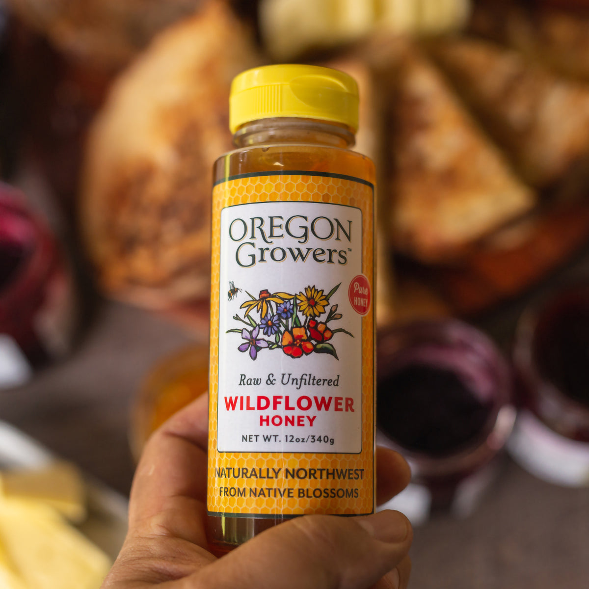 Close-up of a hand holding our 12 oz Oregon Growers Wildflower Honey Squeezable bottle.