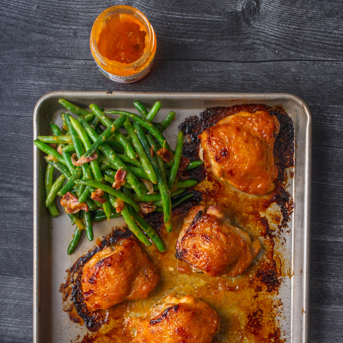 A tin of glazed chicken and beans on a table viewed from the top with Apricot Jam.